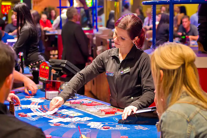 A smiling dealer dealing cards at a blue blackjack-style table while players watch