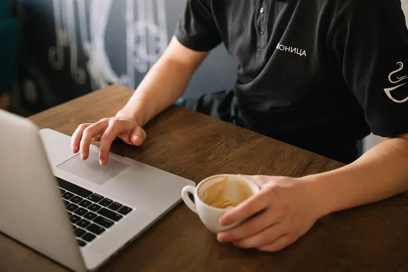 Hands typing on a laptop keyboard next to a cup of coffee